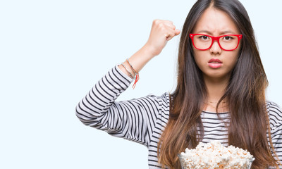 Poster - Young asian woman eating popcorn over isolated background annoyed and frustrated shouting with anger, crazy and yelling with raised hand, anger concept