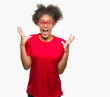 © Krakenimages.com - Young afro american woman wearing glasses over isolated background celebrating crazy and amazed for success with arms raised and open eyes screaming excited. Winner concept