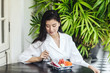 © LUMINA IMAGES - Beautiful Asian woman eating a fruit at terrace.