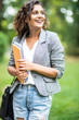 © F8  \ Suport Ukraine - Portrait of a happy mixed race woman student holding books and looking at camera outdoors