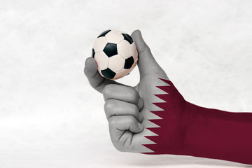 Mini ball of football in Qatar flag painted hand, hold it with two finger on white background. Concept of sport or the game in handle or minor matter.