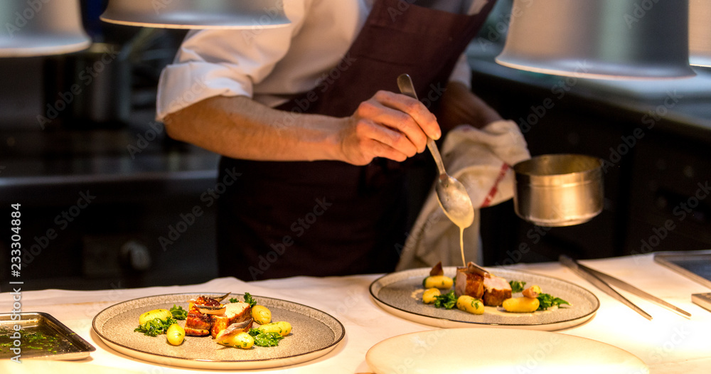 Chef preparing a plate made of meat and vegetables. The chef is pouring sauce on two plates. - obrazy, fototapety, plakaty 