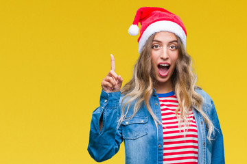 Wall Mural - Beautiful young blonde woman wearing christmas hat over isolated background pointing finger up with successful idea. Exited and happy. Number one.