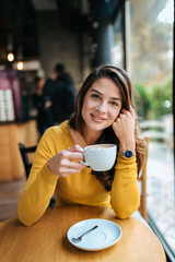 Portrait of a stylish young woman drinking coffee in the cafe, looking at camera.