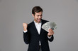 © Drobot Dean - Image of ecstatic businessman 30s in suit smiling and holding fan of money banknotes, isolated over gray background