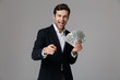 © Drobot Dean - Image of businesslike man 30s in suit smiling and holding fan of money in dollar banknotes, isolated over gray background