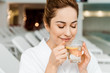 © LIGHTFIELD STUDIOS - happy young woman with closed eyes holding cup with herbal drink and lemon while resting in spa