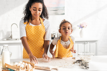 african american mother and daughter preparing dough for dessert in kitchen