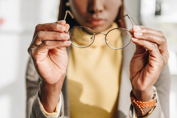 cropped view of african american adult businesswoman in formal wear putting on glasses