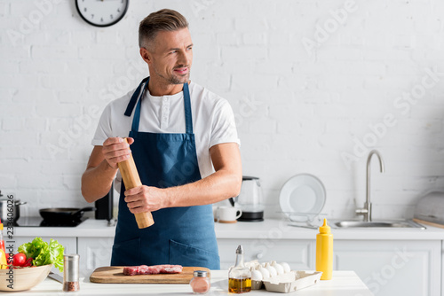 Fotografie, Obraz Smiling man enjoying cooking dinner in kitchen