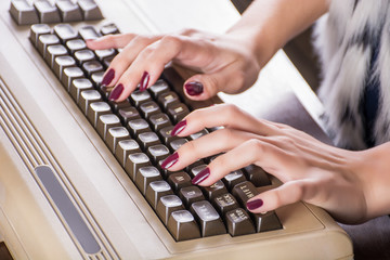 Woman hands typing on old computer keyboard on desk in office. Retro and vintage information technology concept. Close up, selective focus