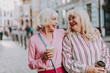 © Yakobchuk Olena - Waist up photo of friends with cardboard cup in hands. White-haired ladies looking in eyes each other