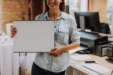 Cropped portrait of charming lady demonstrating blank template for sketch while standing in office and smiling