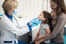 Concept Of Professional Consultation In Healthcare System. Pediatrician Woman Examining Tonsils Of Smiling Little Girl In Medical Office