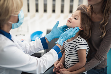 Wall Mural - Concept of professional consultation in therapist system. Pediatrician woman examining tonsils of smiling little girl in medical office