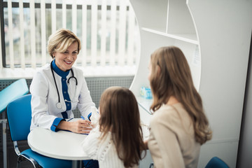 Wall Mural - Concept of positive therapist consultation in healthcare system. Waist up portrait of smiling pediatrician woman making notes while consulting little girl and her mother