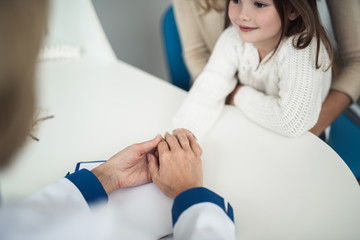 Wall Mural - Concept of positive method of consultation in healthcare system. Top angle portrait of pediatrician woman holding hands of smiling female child while consulting