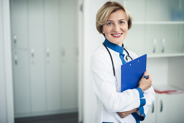 Wall Mural - Concept of professional inspiration in healthcare system. Waist up portrait of smiling female doctor standing in medical cabinet with note holder. Copy space on left