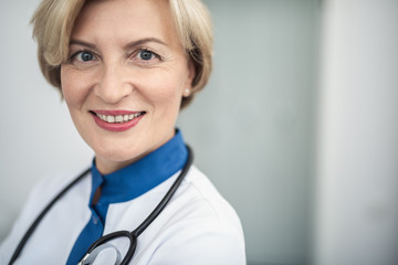 Wall Mural - Concept of professional inspiration in healthcare system. Close up portrait of smiling female doctor in medical uniform confidently standing in cabinet. Copy space on right