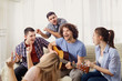 © Studio Romantic - A group of friends with a guitar sing songs at a party indoor