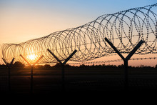 Silhouette Of A Barbed Wire Fence Steel Jail  With The Sunset In The Background