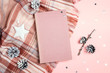 Top-down winter holidays composition with book, plaid, cones and stars on pink background.