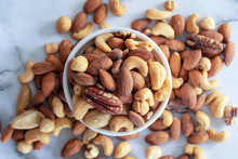 Roasted Mixed Nuts In White Ceramic Bowl On Barble Table Background.