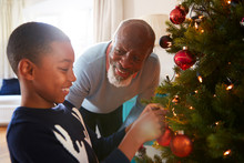 Grandfather And Grandson Hanging Decorations On Christmas Tree At Home Together
