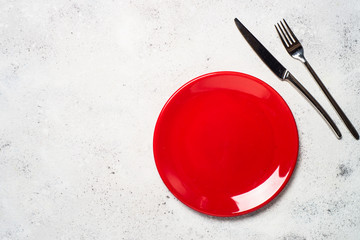 Red plate and cutlery  on light stone table. 