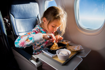 Child eating pancakes in airplane. Little girl having breakfast while flying in aircraft. Blue sky and sun outside the window