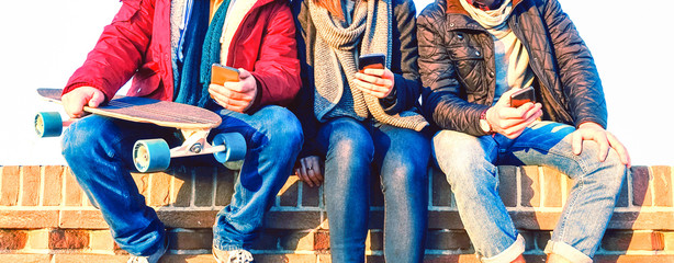 Group of friends using mobile phone sitting in row at winter time - Young people texting on smartphone - Teenagers holding cellphone outdoor - Concept of teens addicted to modern technology