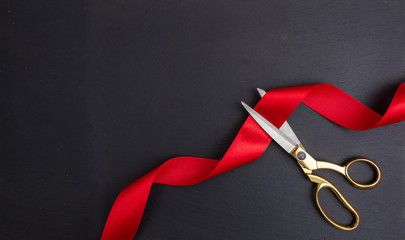 Scissors cutting red silk ribbon against black background