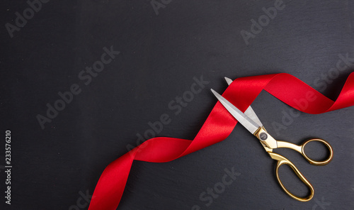 Cuadros en Lienzo Scissors cutting red silk ribbon against black background