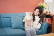 © linghaa - Cheerful young woman holding her puppy with black nose. Indoor portrait of smiling girl with dark long hair posing with dog on rose pink color background and blue sofa at home.
