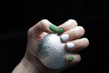 The Green White Manicure Holding Silver Christmas Ball Decoration On Black Background. Isolated Fashion Concept.