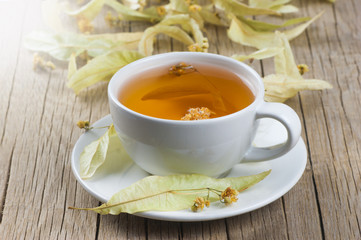 white cup linden tea or blooming tilia, basswood, on rustic vintage wooden table. Herbal tea concept, selective focus
