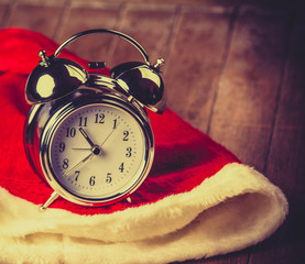 Wall Mural - Metal alarm clock with bell on Santa Claus hat on wooden background