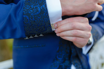 Wall Mural - Businessman in a stylish blue suit with patterns adjusts the cuffs of his shirt. Stylish man in an expensive suit and tie and jacket, close-up. Unrecognizable.