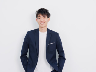 Portrait of handsome Chinese young man in dark blue leisure suit posing against white wall background. Hands in pocket and smiling at camera, looks confident.