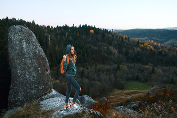 Wall Mural - smiling woman hiker with backpack standing on edge of cliff against a forest background