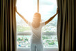 Morning of a new day woman wake up in the bedroom with her refreshing. She stand at the window , raised her two arms and look city view get sunlight