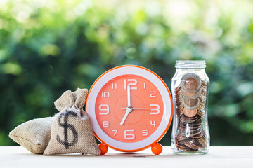 Wall Mural - Stacking growing coins, Moneybags and orange clock on wooden table.