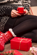 A Small Red Cup With Hot Chocolate And Marshmallows In The Hands Of A Woman In Red Warm Socks Sitting Among Packed Christmas Gifts