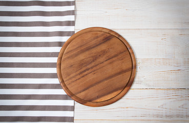 Wall Mural - Round pizza cutting board and striped tablecloth on white wooden background. Top view. Copy space and mock up.