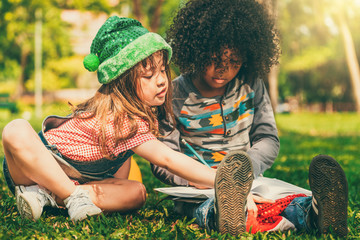 School boy and girl reading book together in park.