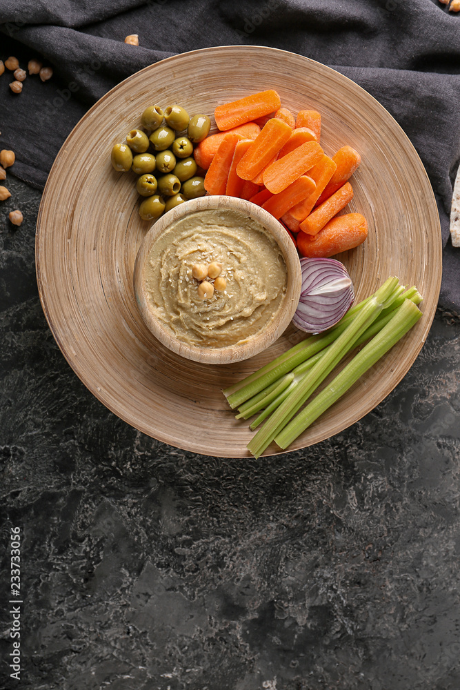 Bowl with tasty hummus and vegetables on dark table