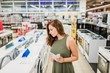 © bnenin - Woman buys washing machine in a store, holding manual.