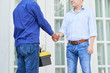 © DragonImages - Repairman in uniform with toolbox shaking hands with house owner near the of the house