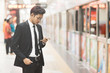 © Hafiez Razali - Young hipster asian businessman using smartphone while waiting for a train in subway. Concept of wireless technology, mobile internet and online business