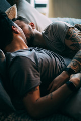 Wall Mural - Caucasian homosexual family in bed before sleep. Handsome hot man with bristle kissing good night his sleepy male partner, lying in bed